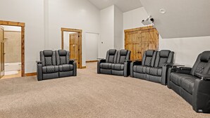 Una sala de cine en casa con tres sillones reclinables negros, un ventilador de techo y un proyector montado en la pared.