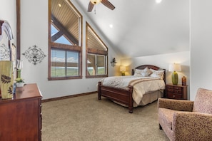 A bedroom with a sloped ceiling, a bed, a nightstand, a lamp, a chair, and a dresser.