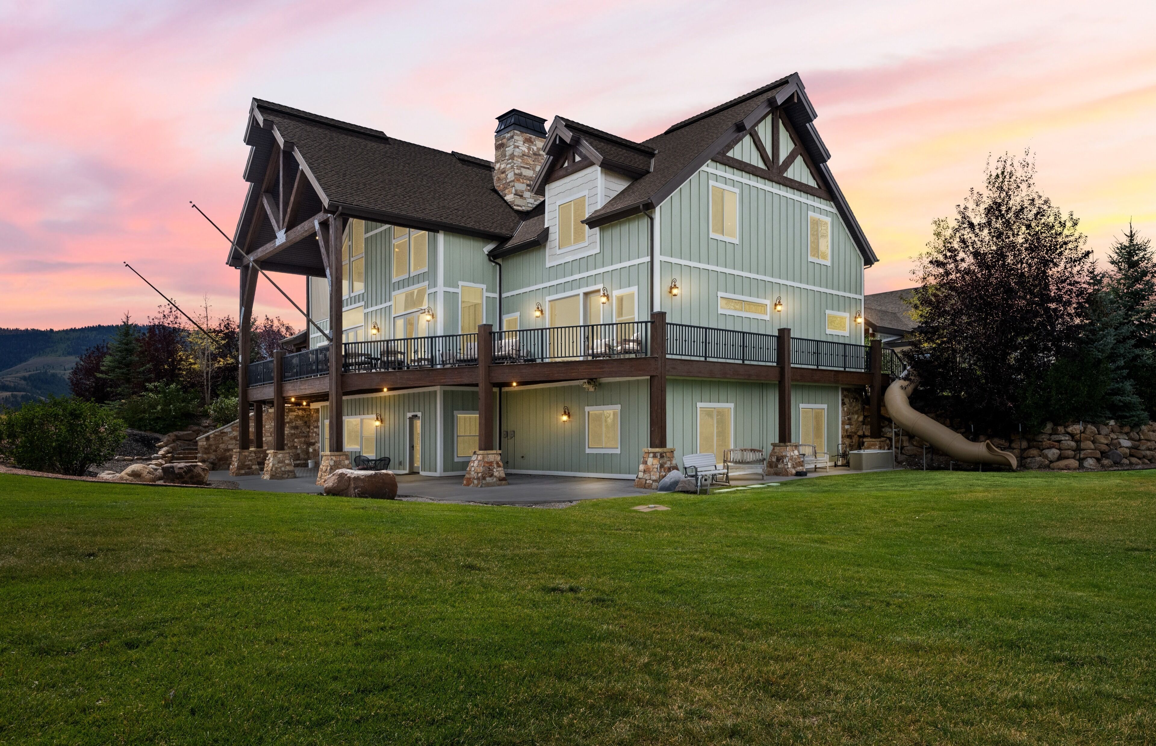 A large, multi-story house with a prominent stone chimney, a balcony, and a well-maintained lawn.