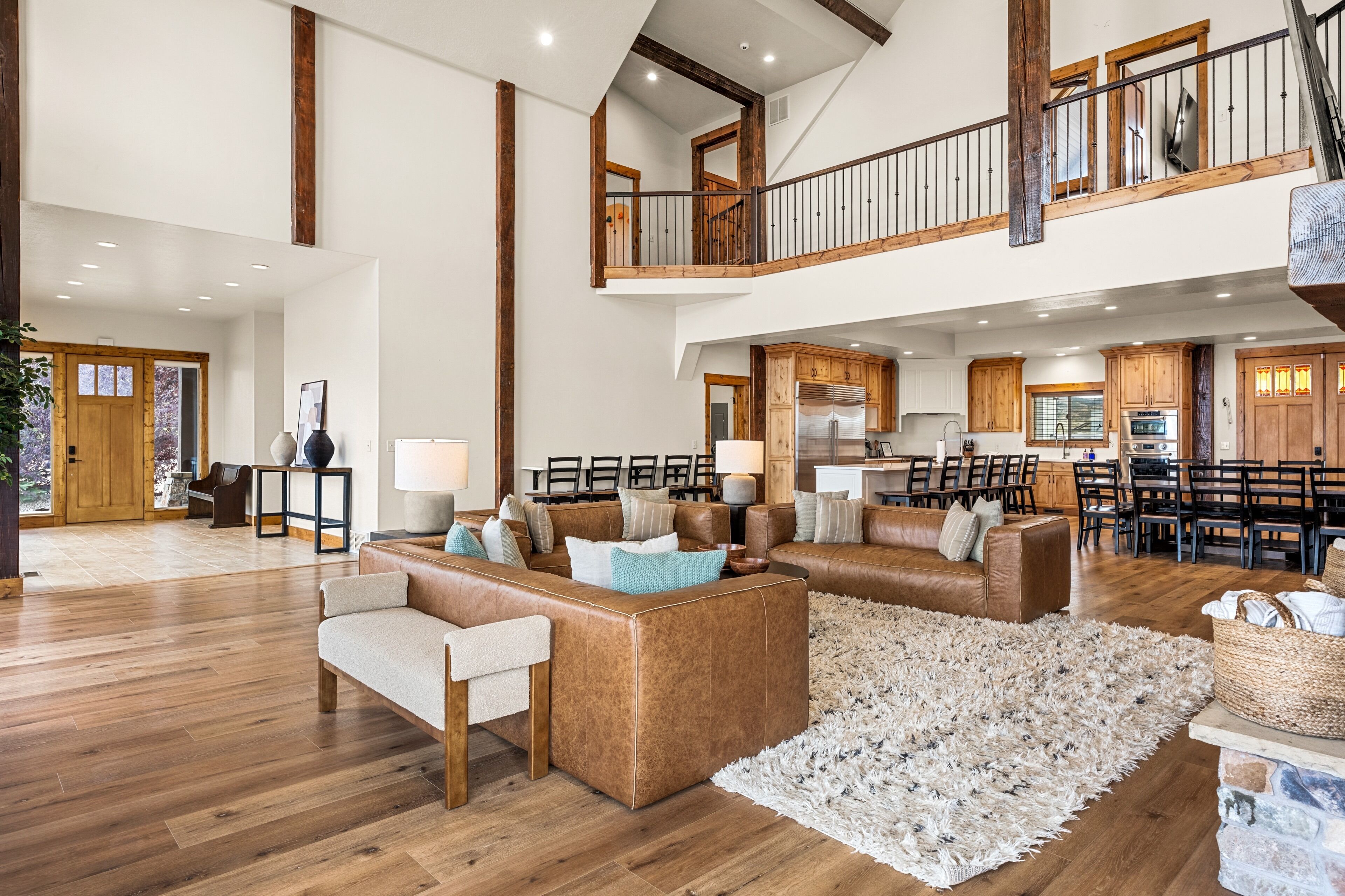 A spacious living area with a high ceiling, wooden beams, a dining area with multiple chairs, and a kitchen with modern appliances.