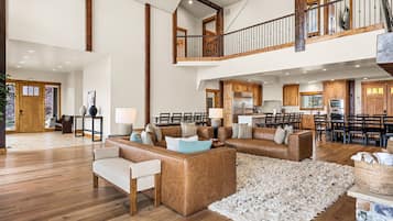 A spacious living area with a high ceiling, wooden beams, a dining area with multiple chairs, and a kitchen with modern appliances.