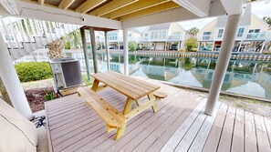 A covered outdoor area with a wooden picnic table, a pool, and a view of residential buildings. - Sandpiper Cove 0013 3 Bedroom Villa (Destin)