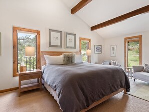 Une chambre à coucher avec un grand lit, des tables de chevet, une chaise et des œuvres d’art encadrées accrochées aux murs.