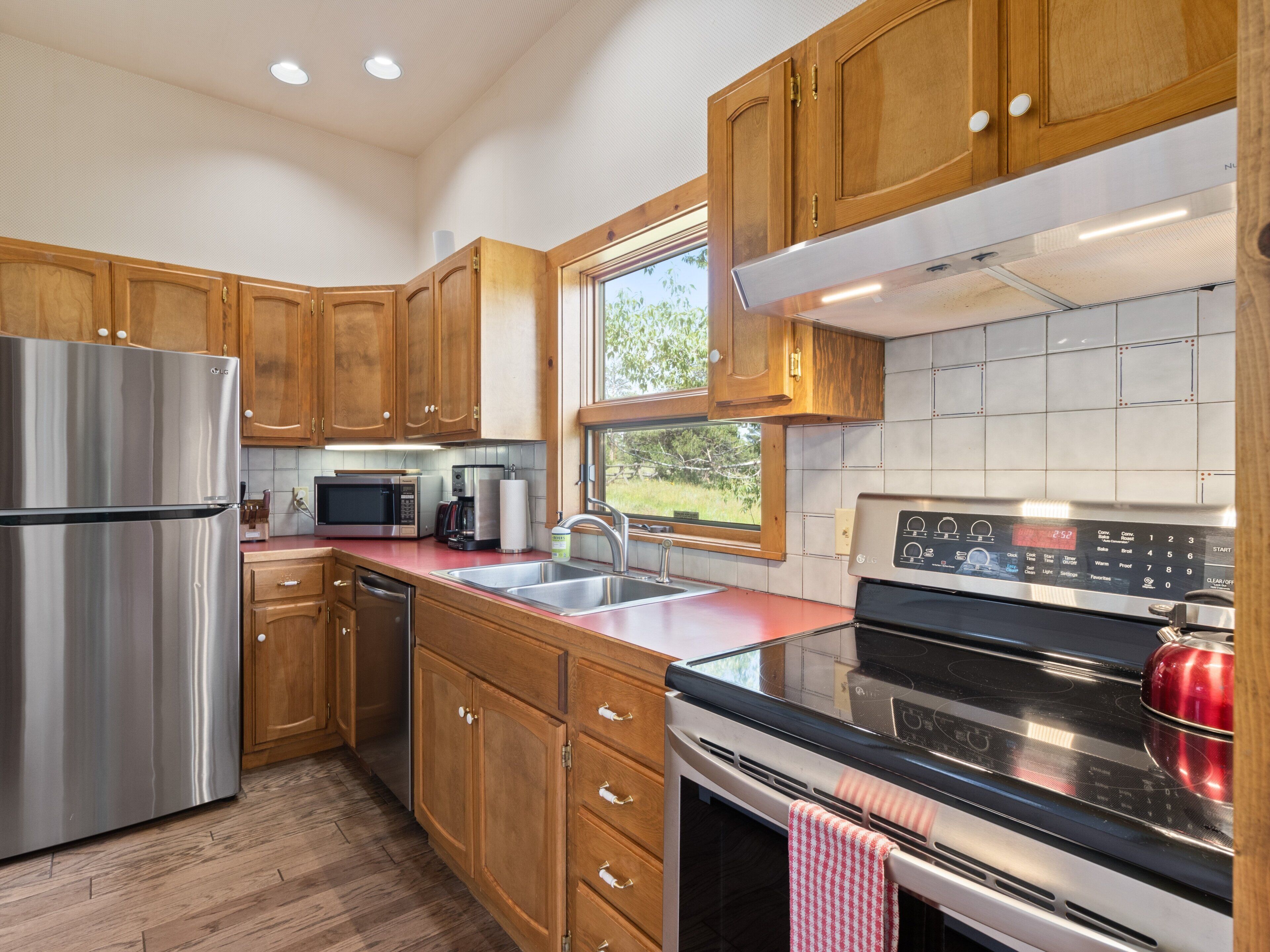 Una cocina moderna con armarios de madera, electrodomésticos de acero inoxidable, una ventana y un salpicadero de azulejos.