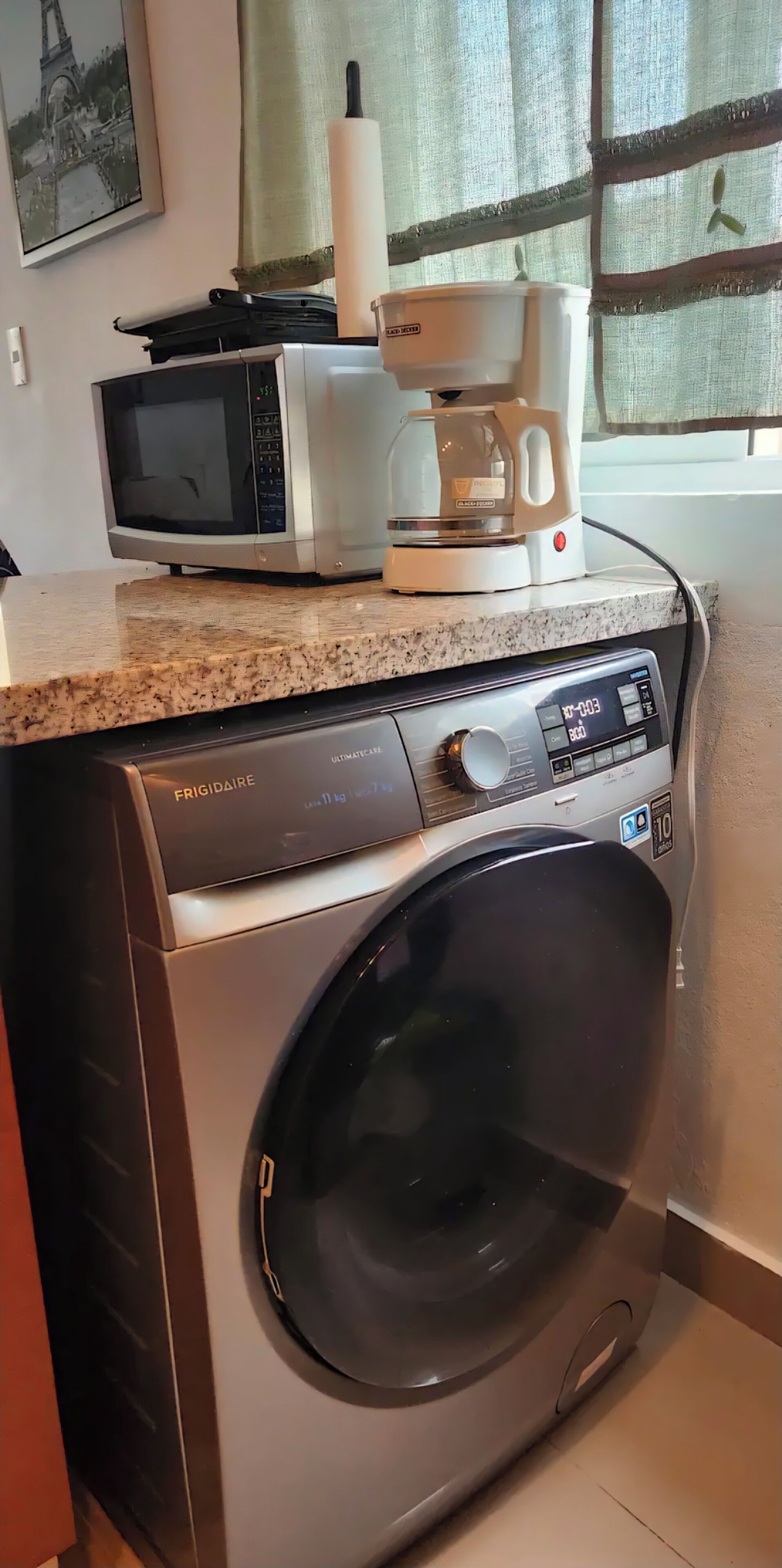 A compact kitchen with a washing machine, microwave, and coffee maker on the countertop.