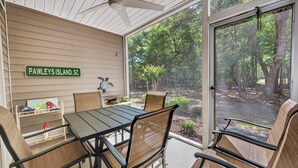 A covered patio with a table and chairs, a ceiling fan, and a view of a wooded area. - 77b Coastal Fairway 3 Bedroom Condo (Pawleys Island)