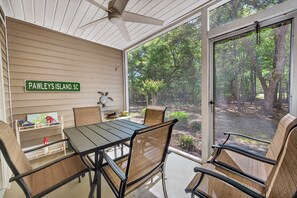 A covered patio with a table and chairs, a ceiling fan, and a view of a wooded area. - 77b Coastal Fairway 3 Bedroom Condo (Pawleys Island)
