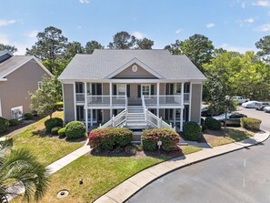 A two-story house with a front porch, a driveway, and a parking lot. - 77b Coastal Fairway 3 Bedroom Condo (Pawleys Island)