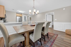 A dining area with a wooden table, beige chairs, a chandelier, and a patterned rug. - 77b Coastal Fairway 3 Bedroom Condo (Pawleys Island)