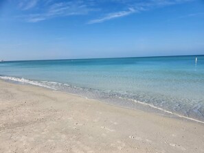 Ein Strand mit klarem Wasser, sandigem Ufer und blauem Himmel.