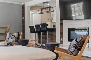 Ein modernes Wohnzimmer mit einer großen Couch, einem Essbereich mit Tisch und Stühlen, einem Kamin und einer Küchenzeile mit Barhocker.