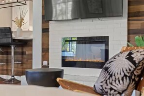 Ein modernes Wohnzimmer mit Kamin, einem darüber hängenden Fernseher und einer Pflanze an der Seite.