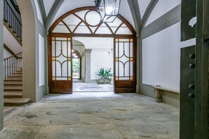 Un pasillo con suelo de piedra, una puerta de madera, una escalera y una planta en maceta.