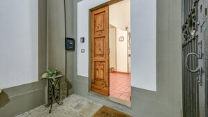 Een hal met een houten deur, een kleine tafel met een plant, een welkomstmat en een beveiligingscamera.