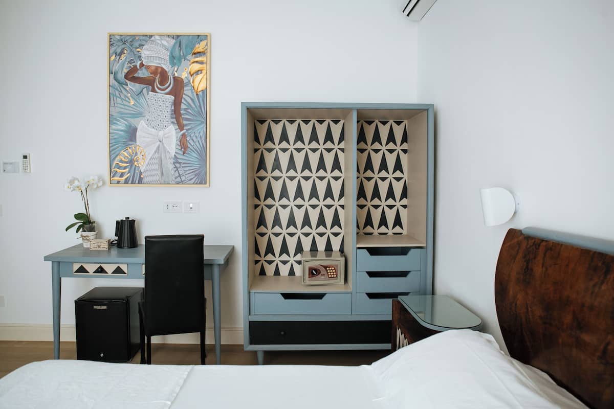 Habitación de hotel con cama, escritorio, silla, armario y un cuadro en la pared.
