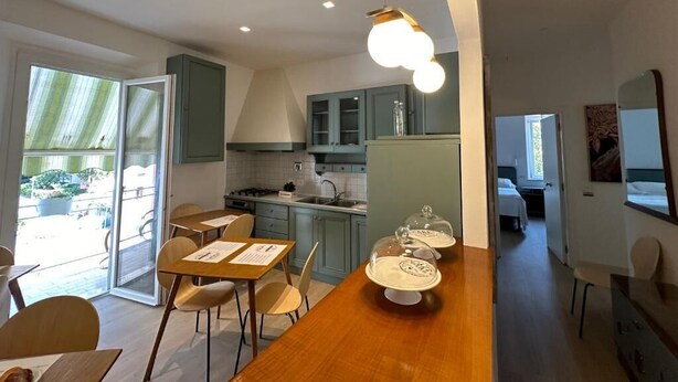 A modern kitchen with a dining area, a view to the outside, and a small seating area. - Domus Socolatae Cocoa Journey  (Follonica)