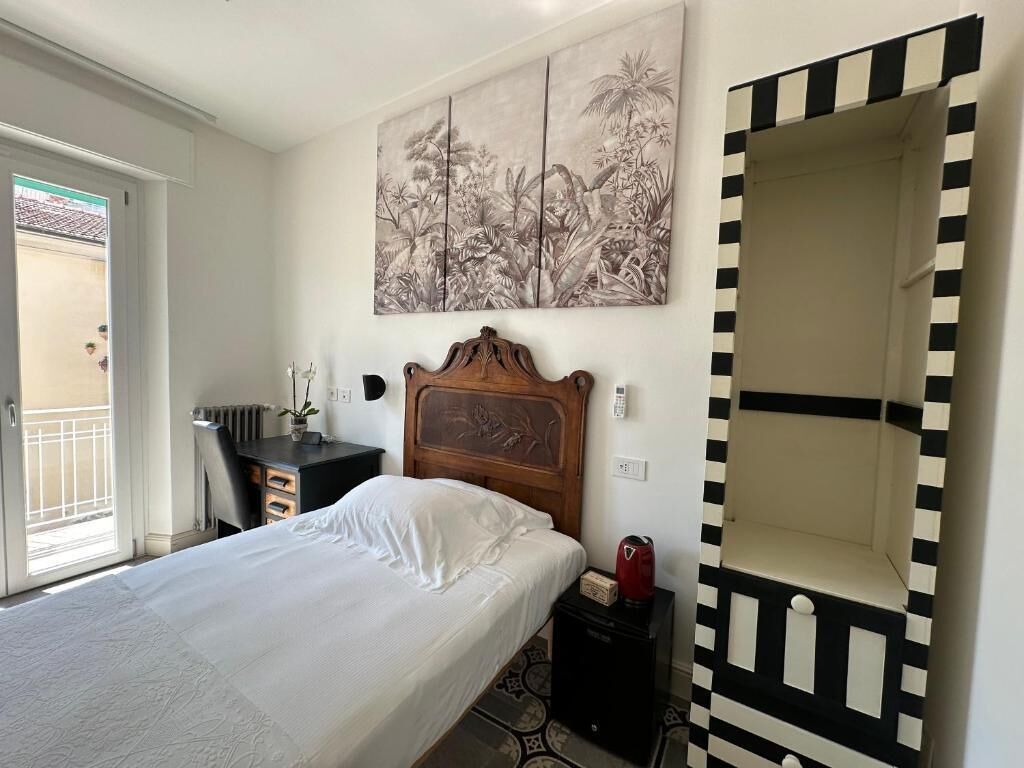 A bedroom with a bed, a desk, a chair, a radiator, a painting, and a mirror.