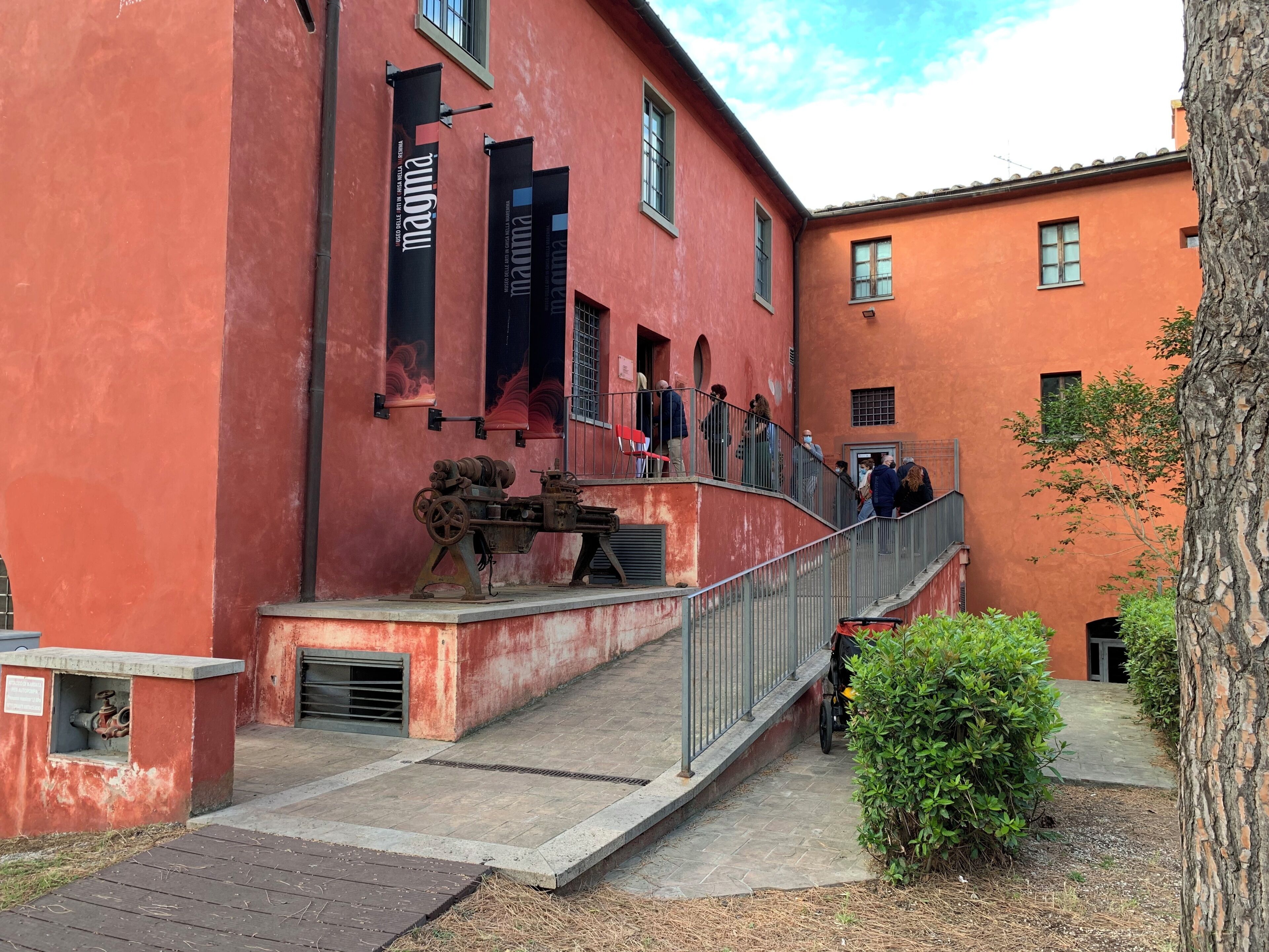 A building with a red facade, a staircase leading to a balcony, and a tree in the foreground.