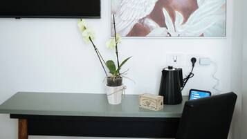 A desk with a potted plant, a coffee maker, and a smartphone charging.