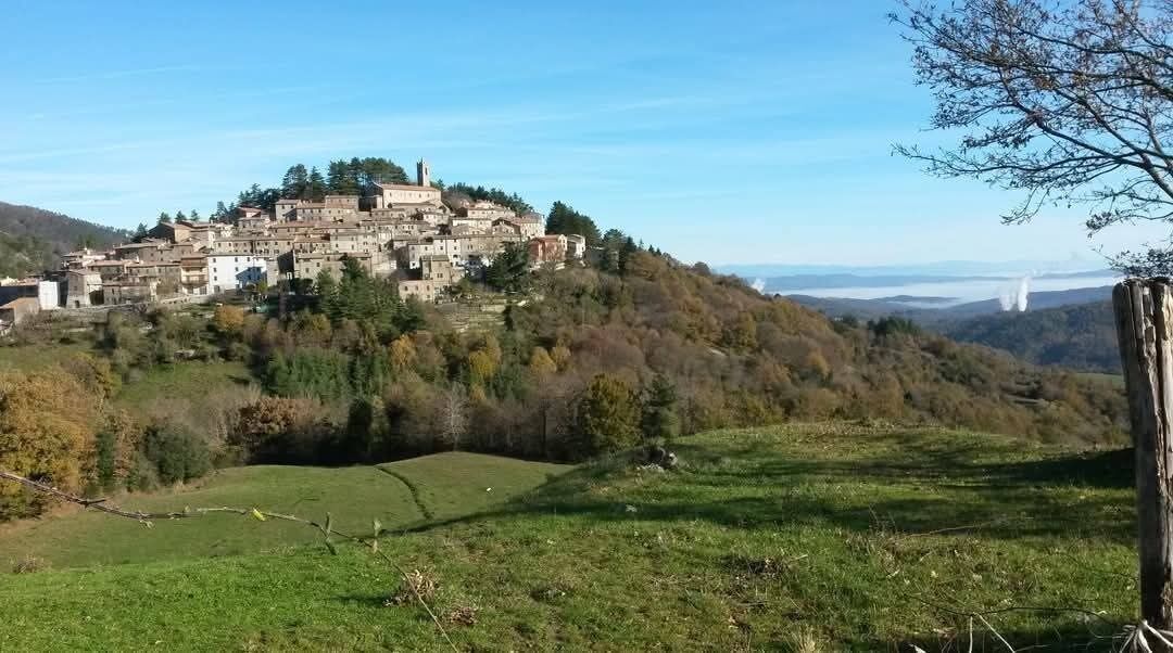 Ein Dorf an einem Hang mit traditionellen Steinhäusern, blauem Himmel und Blick auf ferne Berge.