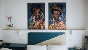 A hotel room with a bed, a nightstand, a desk, a chair, two paintings, and a potted orchid. - Domus Socolatae Cocoa Journey  (Follonica)