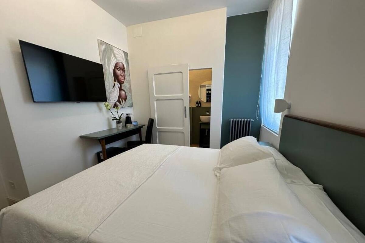 Habitación de hotel con cama, televisor de pantalla plana en la pared, escritorio con silla y puerta que da a un baño.