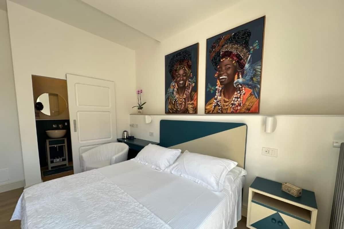 Un dormitorio con cama, mesita de noche, cómoda, espejo y dos cuadros colgados en la pared.