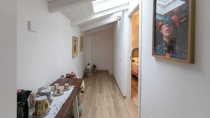 A narrow hallway with a wooden floor, a table with cups and a kettle, and a framed picture on the wall. - IL GIARDINO SEGRETO (Castelfidardo)