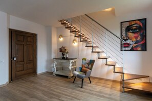 A modern interior with a wooden floor, a staircase with metal railings, a white ornate table, and a colorful abstract painting. - IL GIARDINO SEGRETO (Castelfidardo)