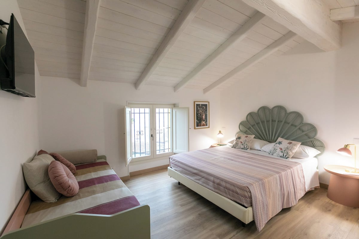 A bedroom with a bed, a sofa, a TV, a window, and a wall-mounted picture.