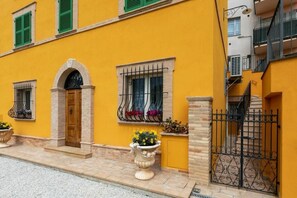 A yellow building with a wooden door, green shutters, and a wrought iron gate. - IL GIARDINO SEGRETO (Castelfidardo)