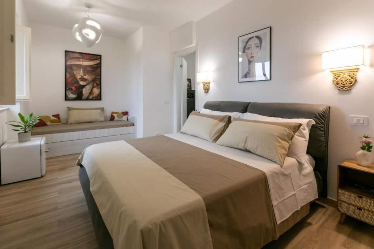 A modern hotel room with a large bed, bedside tables, a small refrigerator, and artwork on the walls.