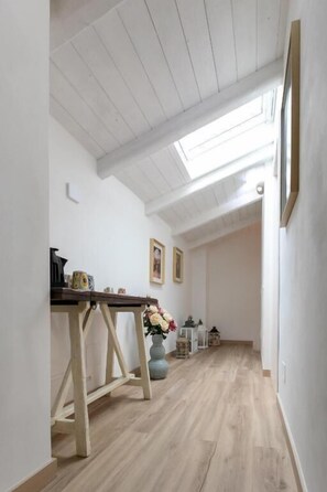 A narrow hallway with wooden flooring, a table with items on it, and a vase with flowers. - IL GIARDINO SEGRETO (Castelfidardo)