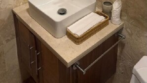 Un baño con pared de mármol, un espejo redondo, un lavamanos blanco, un perchero y una cesta.