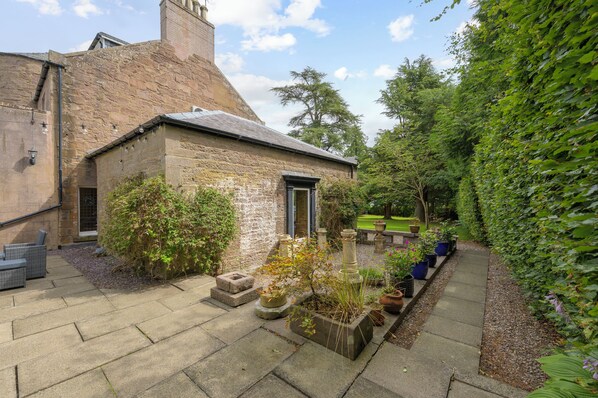 A stone building with a garden patio, outdoor seating, and a variety of potted plants.