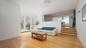A modern living room with a wooden floor, a white sofa with a blue cushion, a wooden coffee table, and a staircase leading to another level.