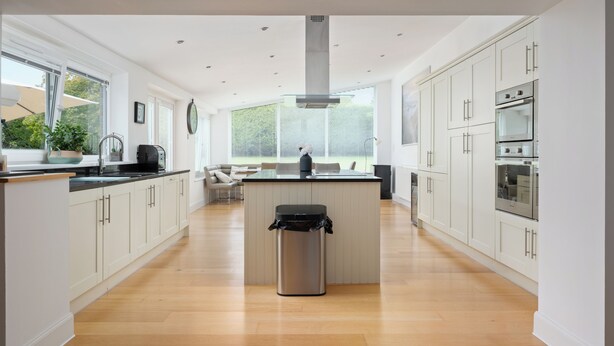 A modern kitchen with white cabinets, a central island, and a stainless steel trash can.