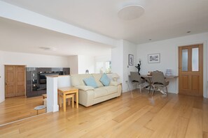 A spacious living area with a sofa, a dining table, and chairs. There is a kitchen area with a refrigerator and cabinets.