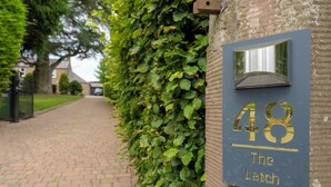 A house number sign with '48 The Latch' on a brick wall, a paved driveway, and a hedge.