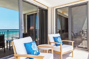 Ein Balkon mit zwei Stühlen und einem Tisch mit Blick auf einen Strand.
