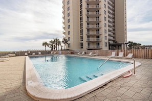 A rectangular swimming pool with a tiled edge, surrounded by lounge chairs and palm trees. - ☀️🌴Beachfront Penthouse w/ Panoramic Views | Pool | Navarre Towers 1202 (Navarre Beach)