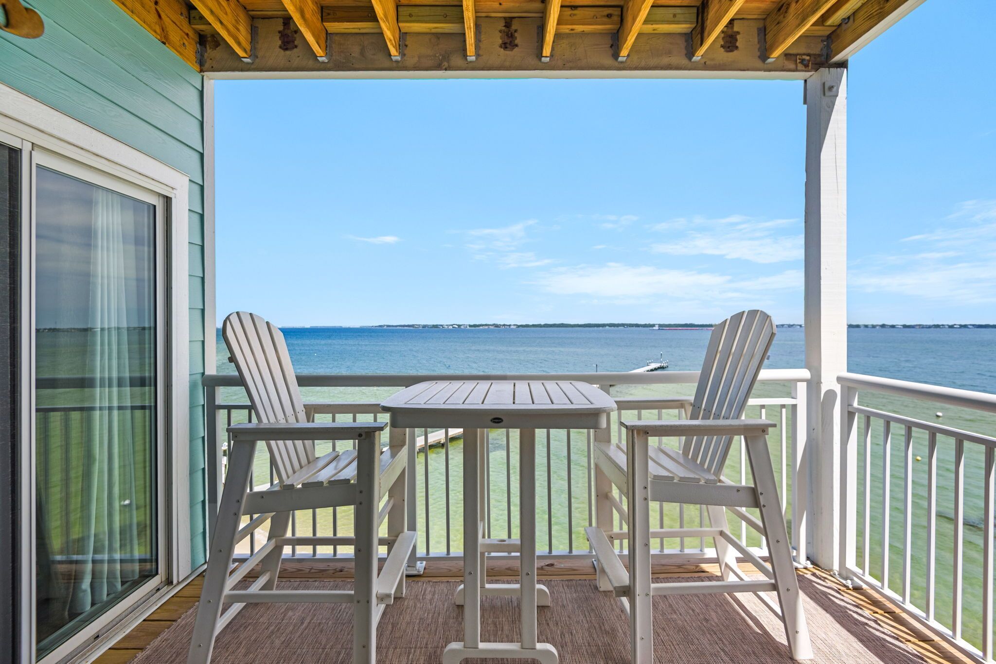 A covered outdoor area with a table and two chairs, overlooking a body of water.