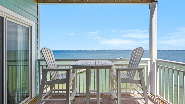 A covered outdoor area with a table and two chairs, overlooking a body of water. - ☀️🩴Stunning Sound Front Views | Community Pool | Walk to Beach | Baywatch E5 (Pensacola Beach)