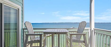 A covered outdoor area with a table and two chairs, overlooking a body of water.