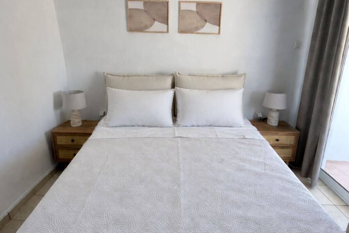 A bed with a white quilt, two bedside tables with lamps, and abstract wall art.