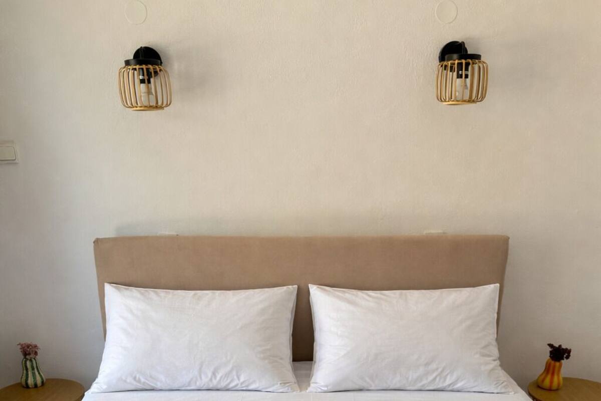 A bed with a beige headboard and two white pillows, a patterned quilt, and two wall-mounted light fixtures.