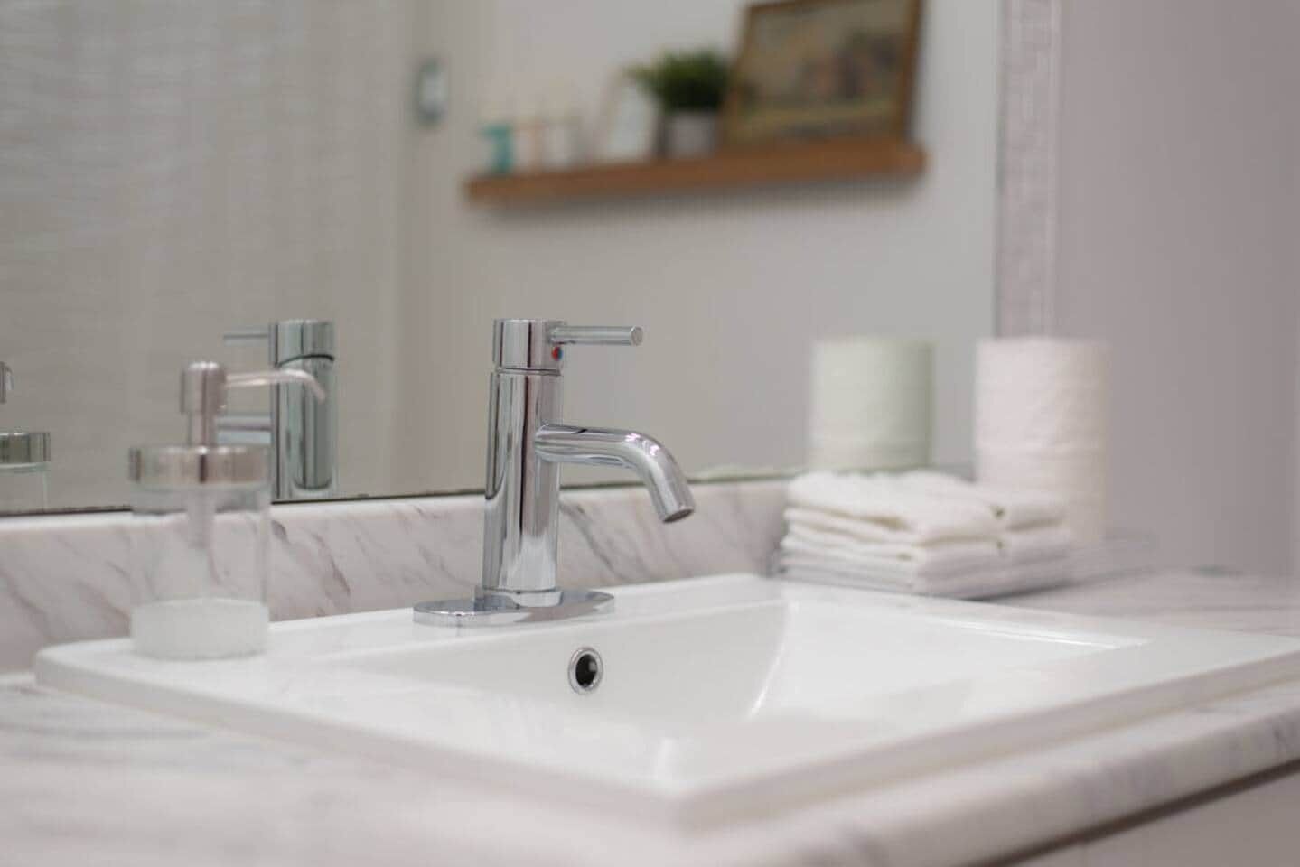 A bathroom with a white sink, two faucets, a mirror, and a stack of white towels.