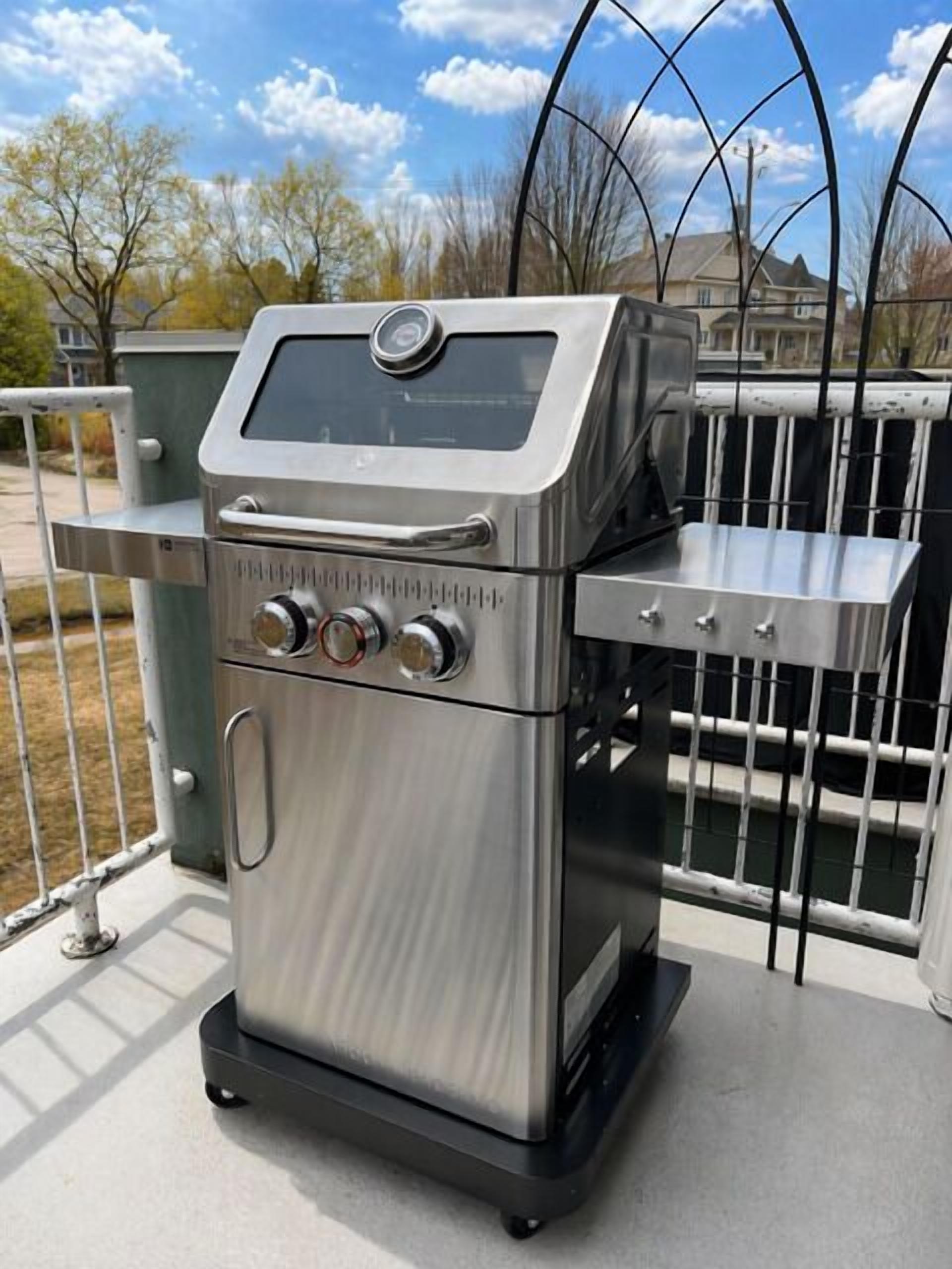 A stainless steel outdoor grill with a digital control panel, a side handle, and a flat top for food.