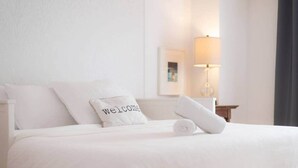 A neatly made bed with a pillow labeled 'Welcome,' a rolled towel, and a bedside lamp. - La Place du Village (Magog)