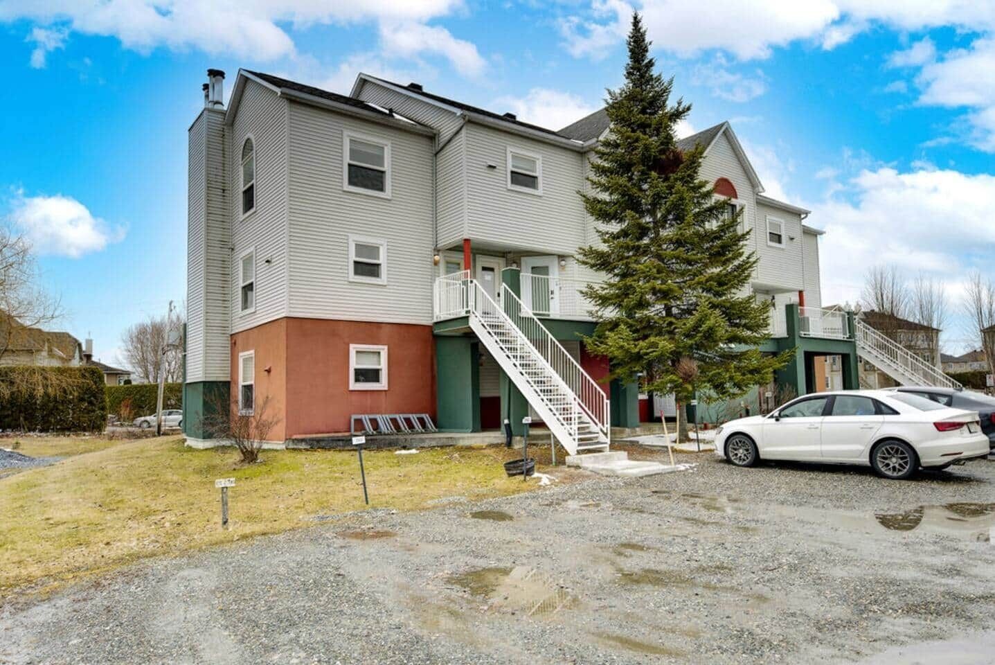 A multi-story building with a staircase, a car parked in front, and a grassy area.